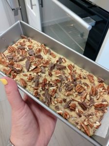 un molde de pan con la masa de plátano y chocolate adentro y nueces troceados encima