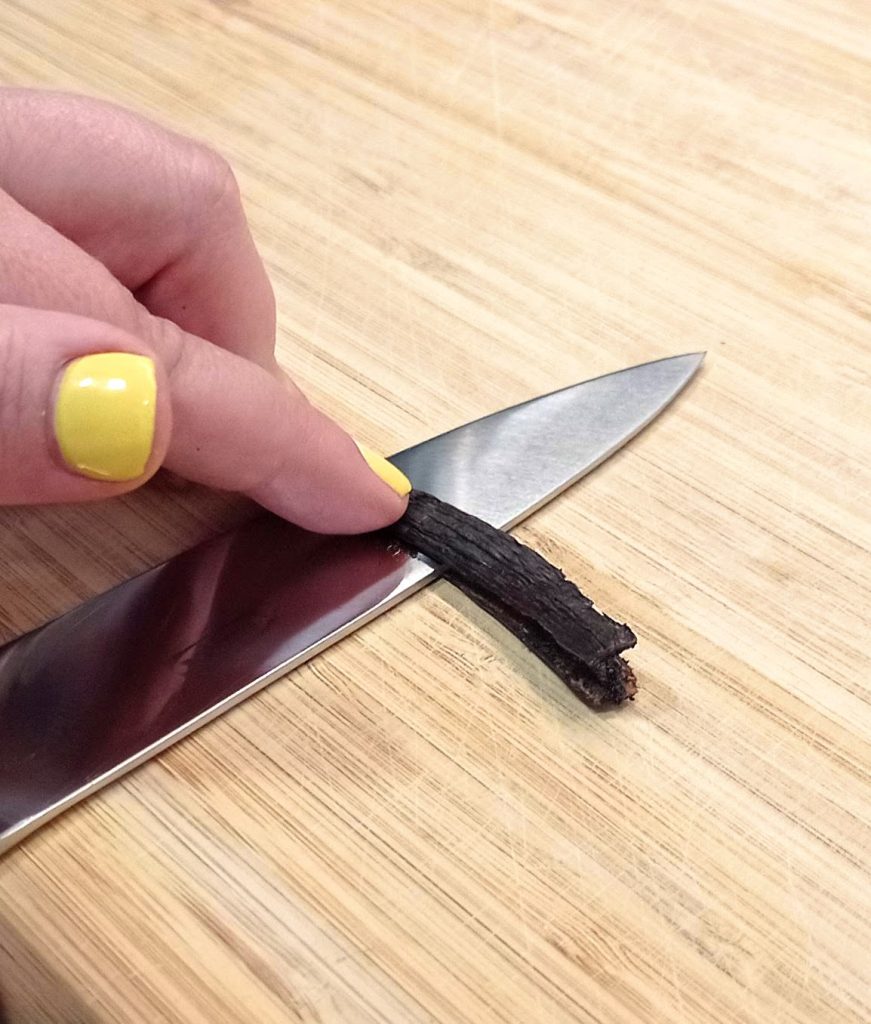 un cuchillo cortando una vaina de vanilla horizontalmente