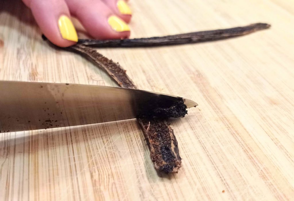 un cuchillo raspando la vaina de vanilla para sacar las semillas