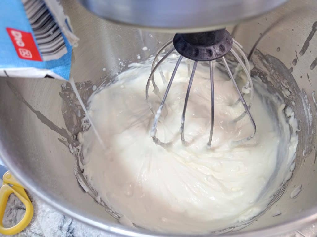 vertiendo la nata para montar en el tazón con el queso cremo y azúcar