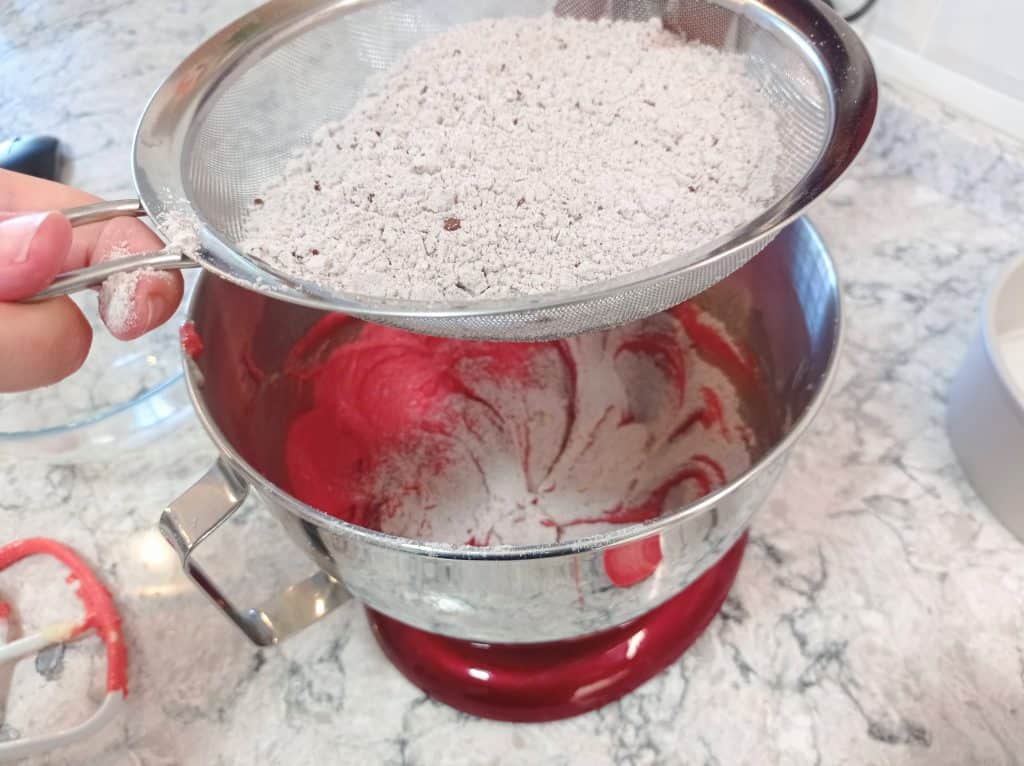 tamizando los ingredientes secos sobre el tazón con la masa de tarta red velvet